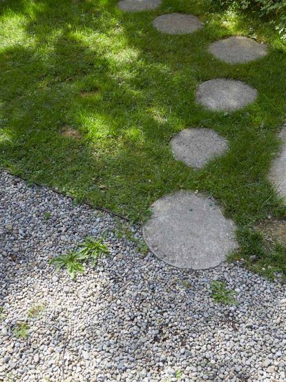 Ein Schrittplattenweg mit runden Betonplatten führt durch den Rasen zum Kiesplatz